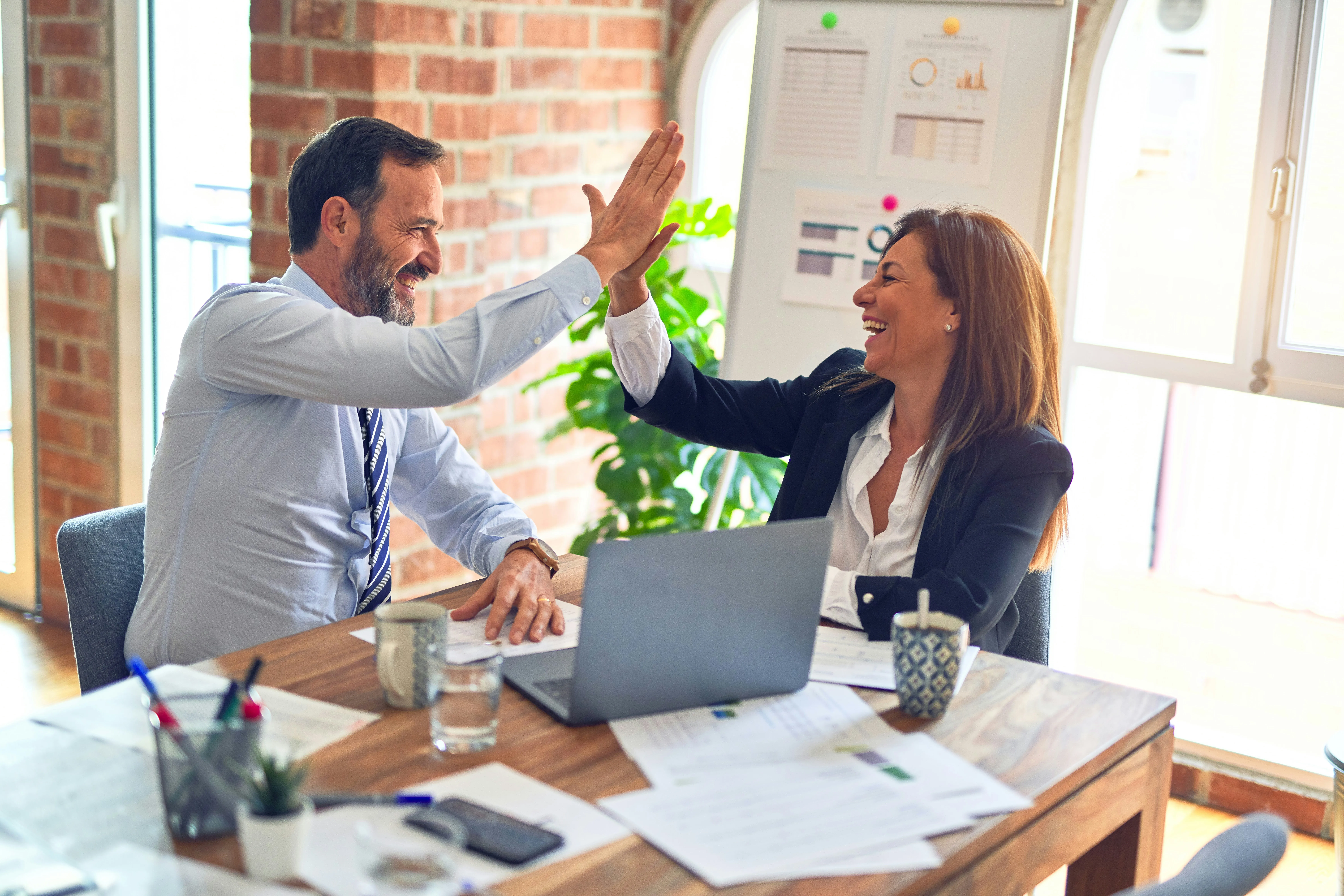 Zwei Kolleg:innen im Büro geben sich ein High-Five am Laptop
